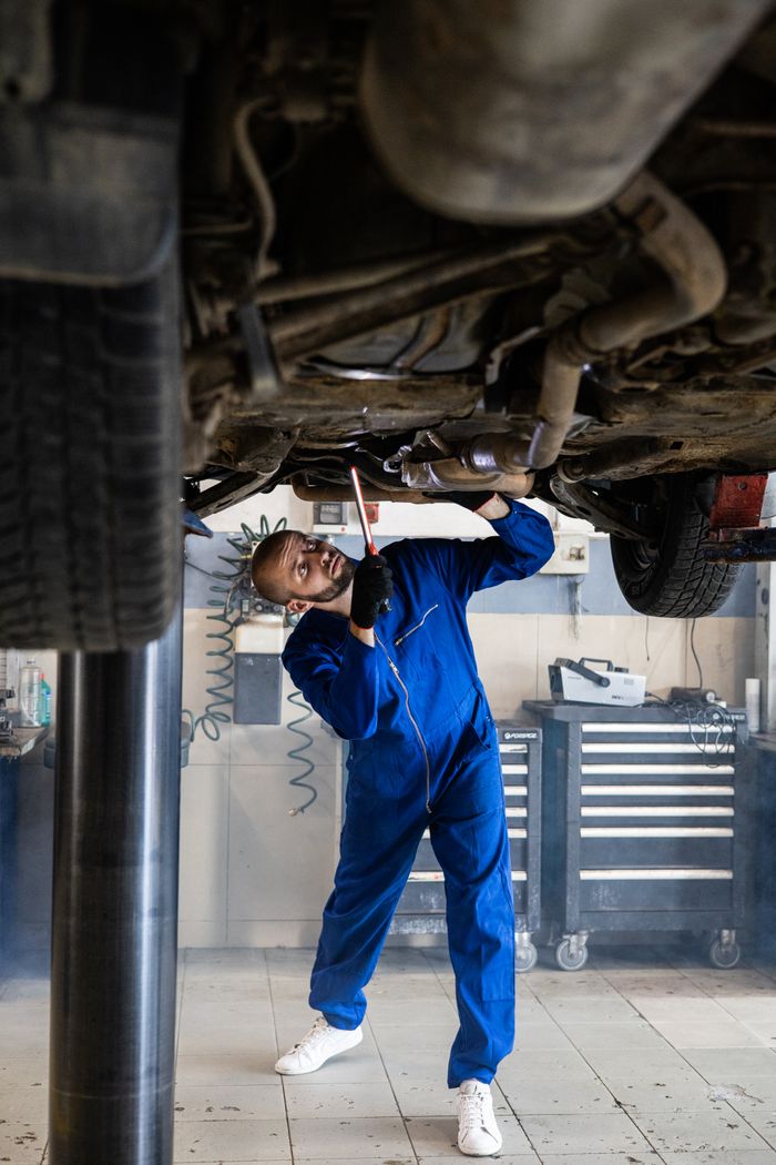 Crafting Captivating Headlines: Your awesome post title goes here A female mechanic in blue coveralls inspects a car's undercarriage in an auto repair shop.