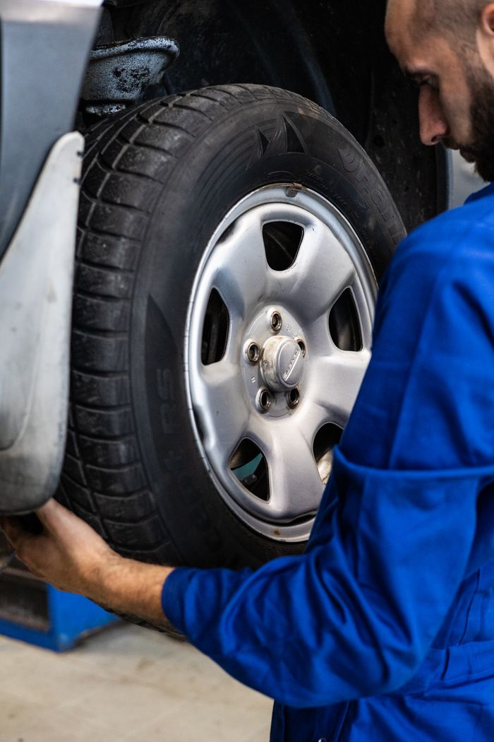 Mastering the First Impression: Your intriguing post title goes here A mechanic in blue uniform closely examines a car wheel for repairs.