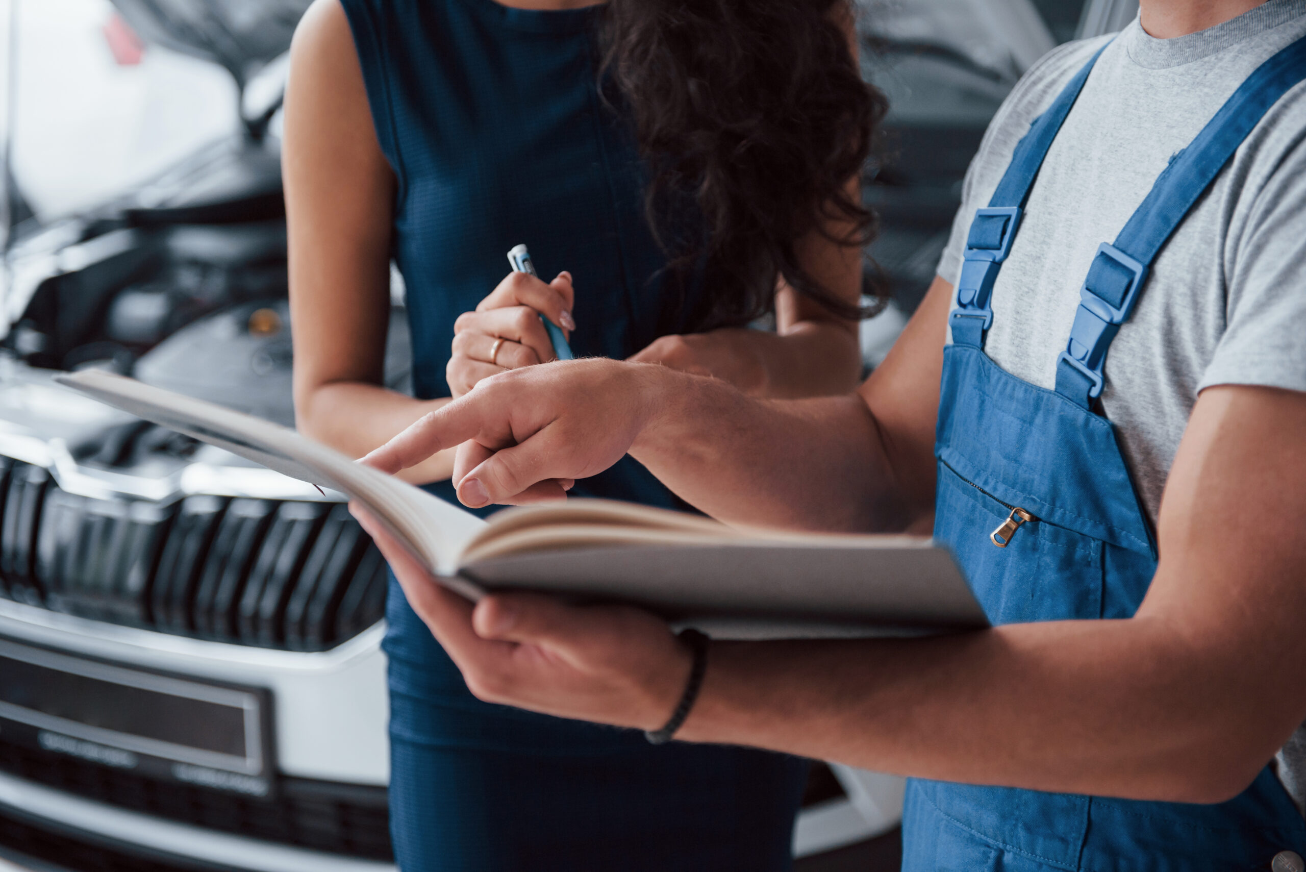 your signature please. woman in the auto salon with employee in blue uniform taking her repaired car back